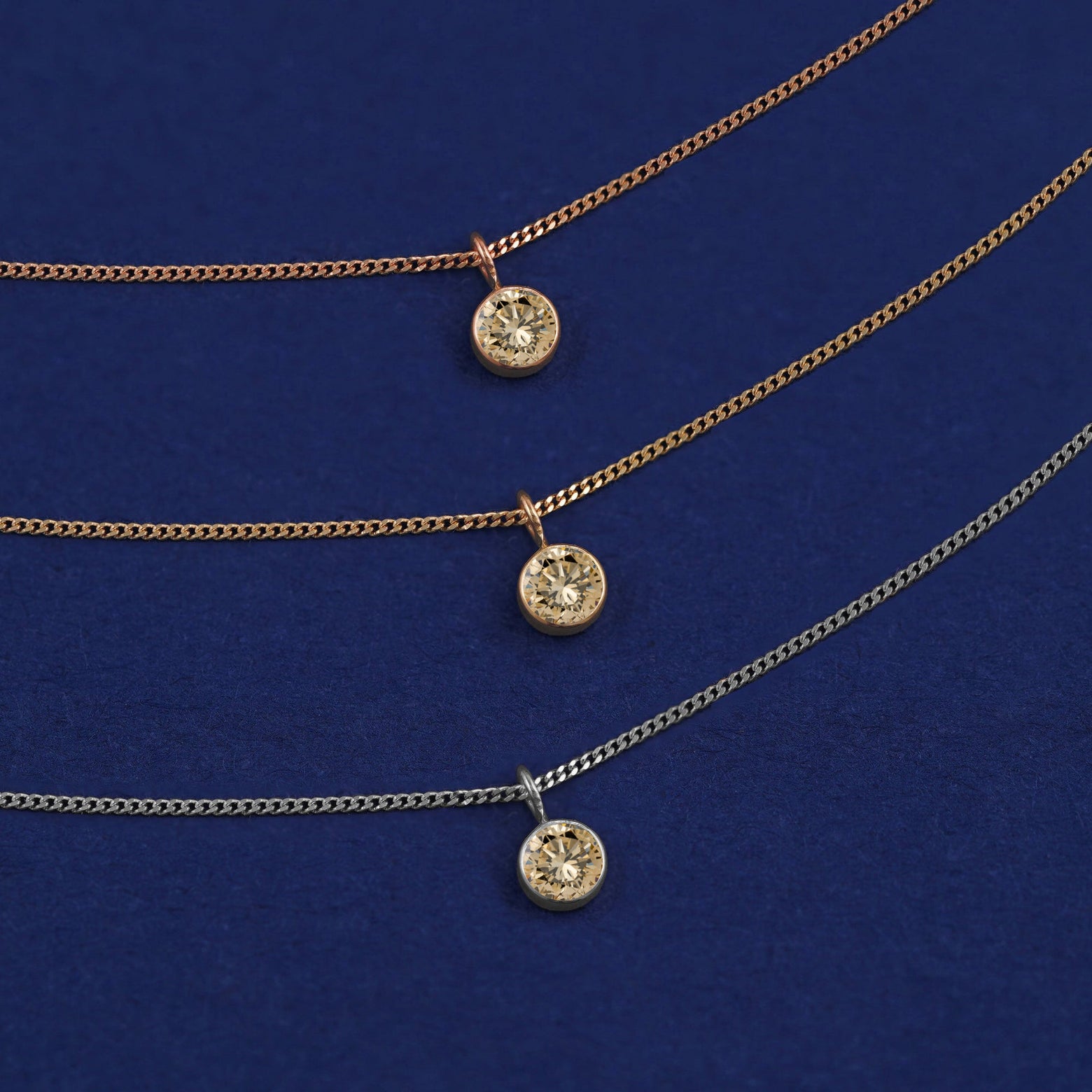 Three versions of the Champagne Diamond Necklace shown in options of yellow, white and rose gold on a dark blue background