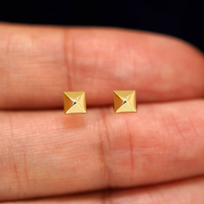 A pair of solid yellow gold Pyramid Earrings in between a model's fingers