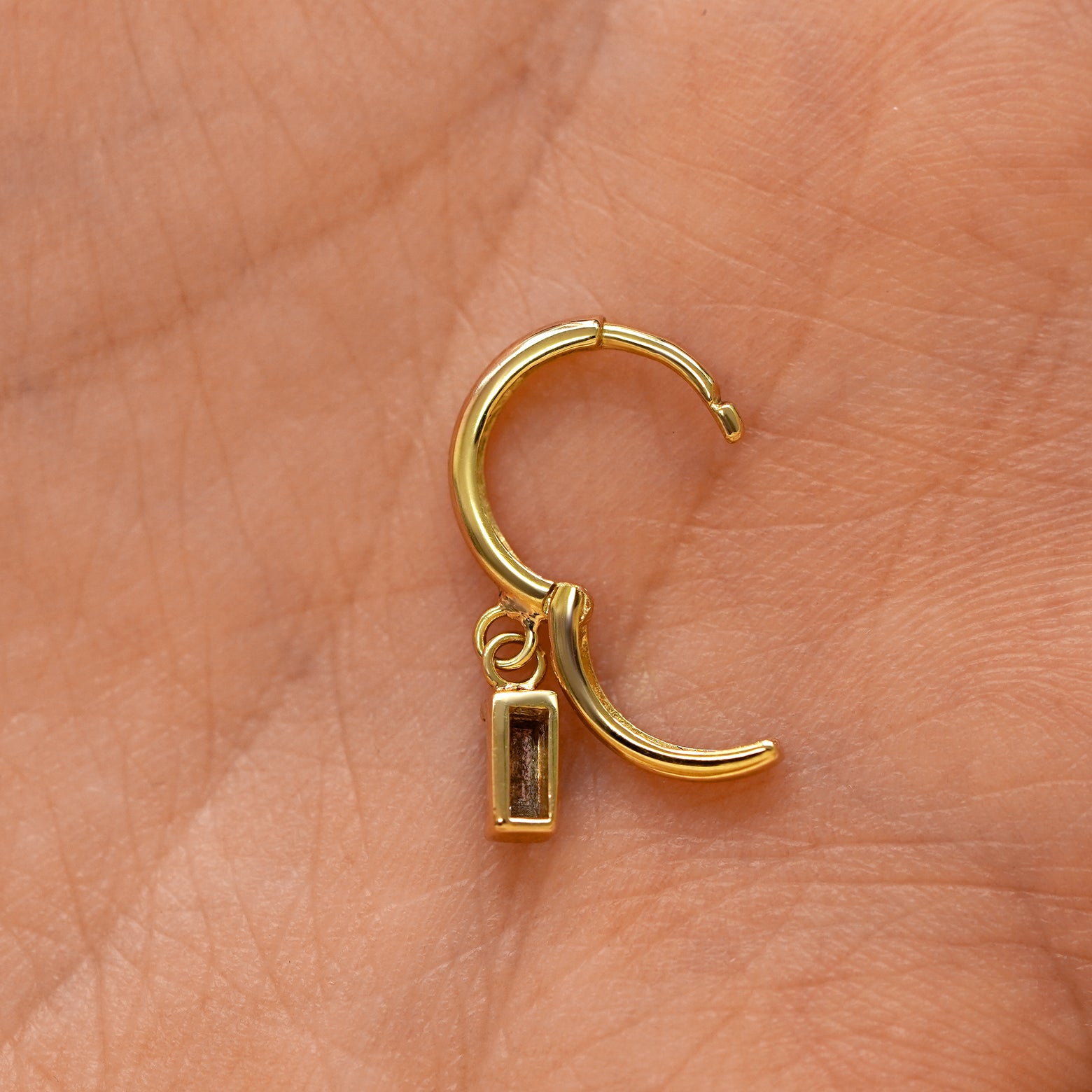 A solid 14k yellow gold Baguette Diamond Dangle Huggie Hoop Earring open a model's palm