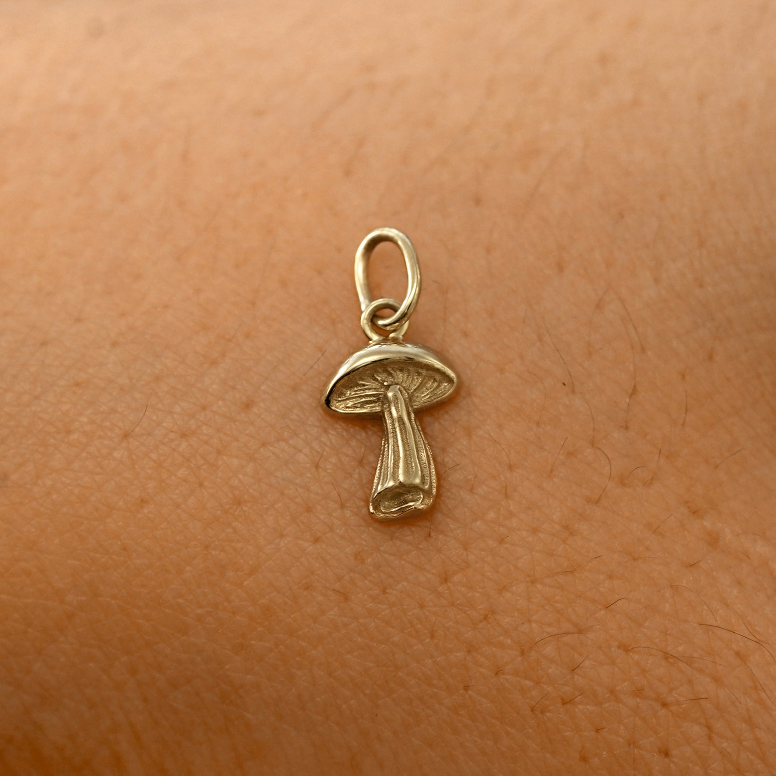 A solid 14k champagne gold Mushroom Charm resting on the back of a model's hand