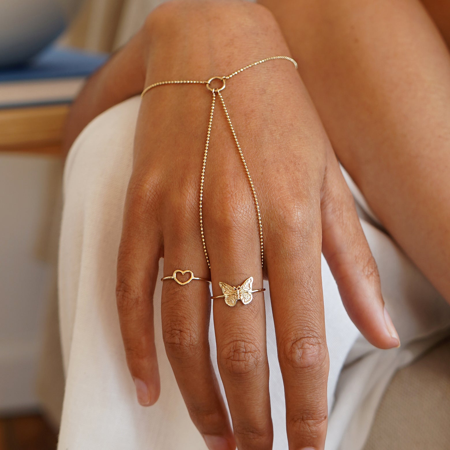 A model with their hand draped over their knee wearing a hand bracelet, a heart ring, and a butterfly ring