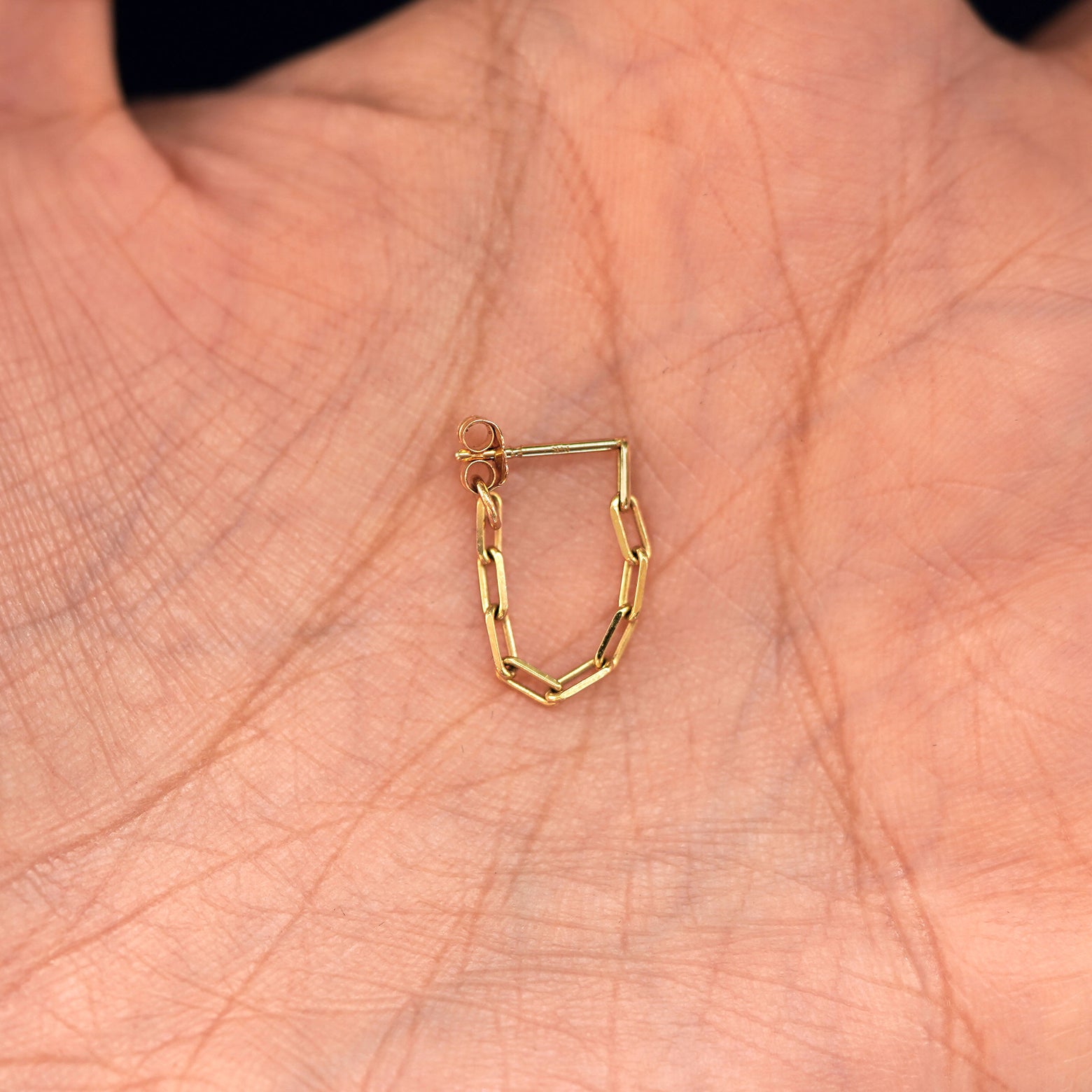 A solid yellow gold Butch Chain Loop with the backing attached to post sitting in a model's hand