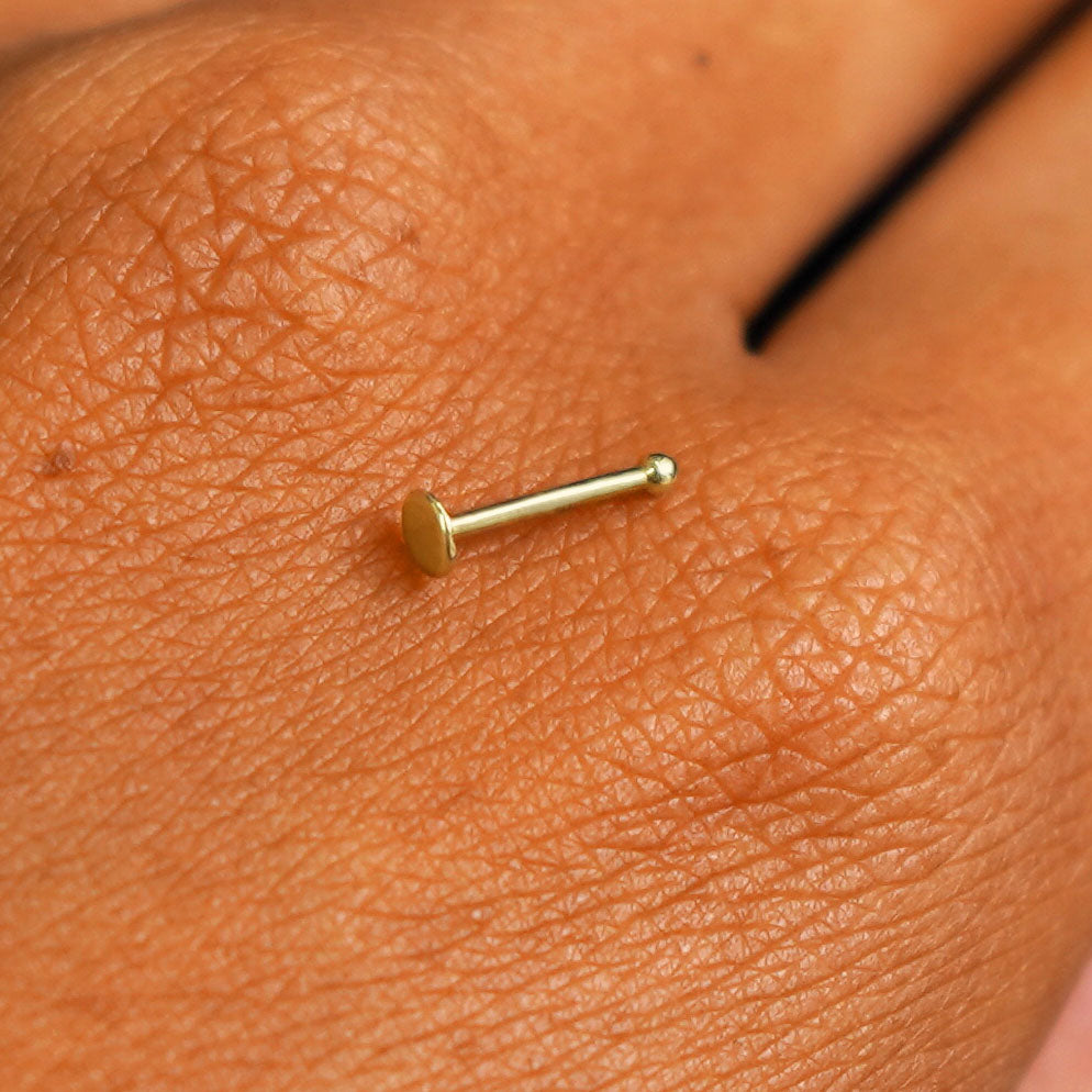 Close up view of a single 14k solid gold Circle Nose Stud resting on the back on a model's hand