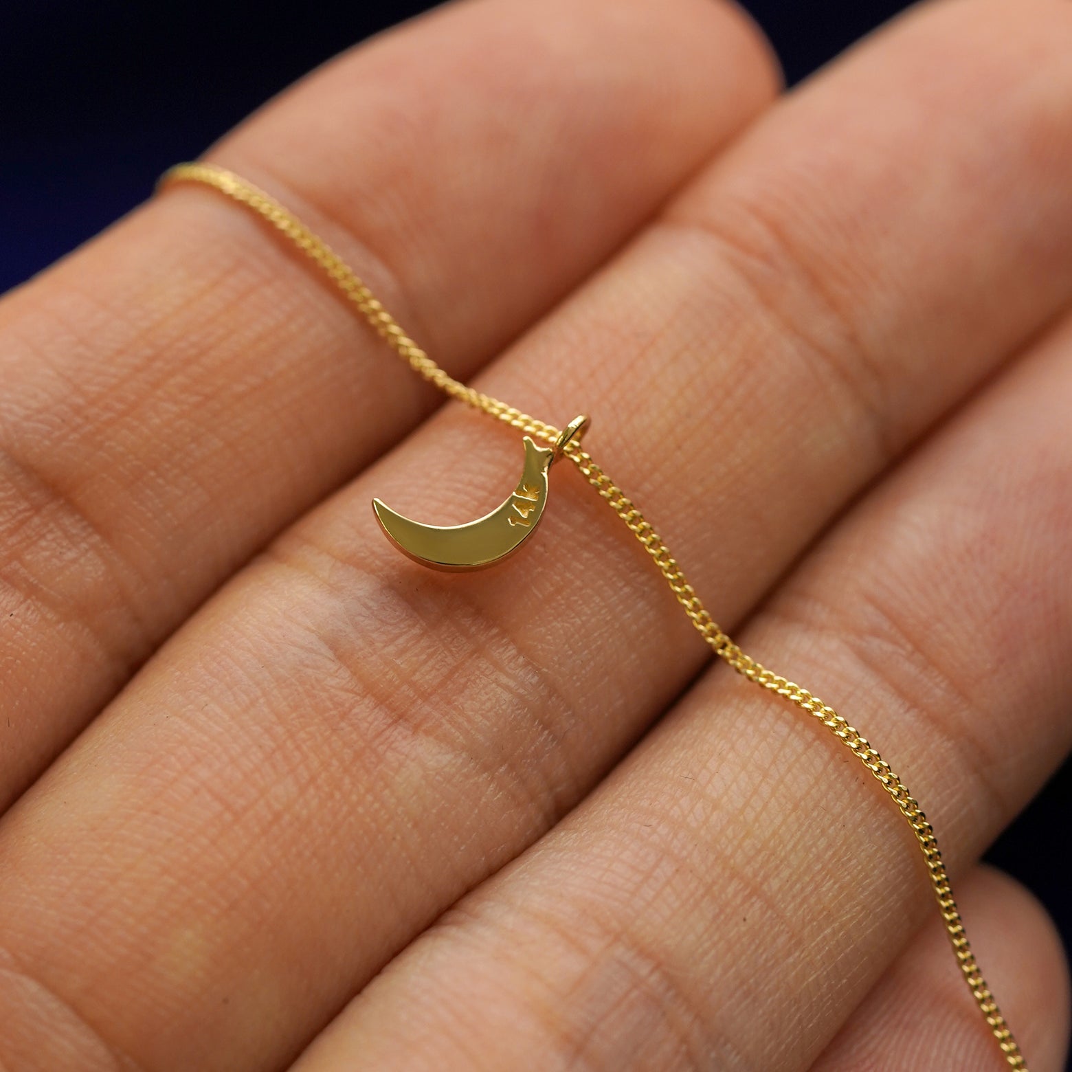 Back side view of a 14k gold moon pendant necklace lying across a model's fingertips