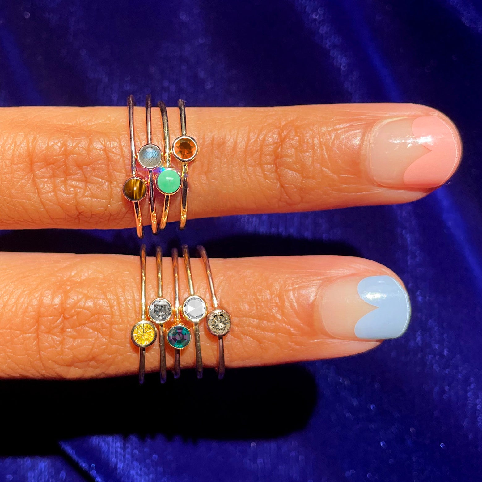 Two fingers with cool nail polish wearing various Automic Gold rings including a Fire Opal Ring