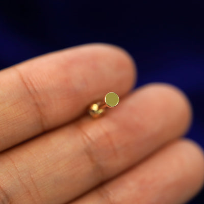 A solid yellow gold Aquamarine Flatback Piercing laying facedown on a model's finger to show the end of the flat back