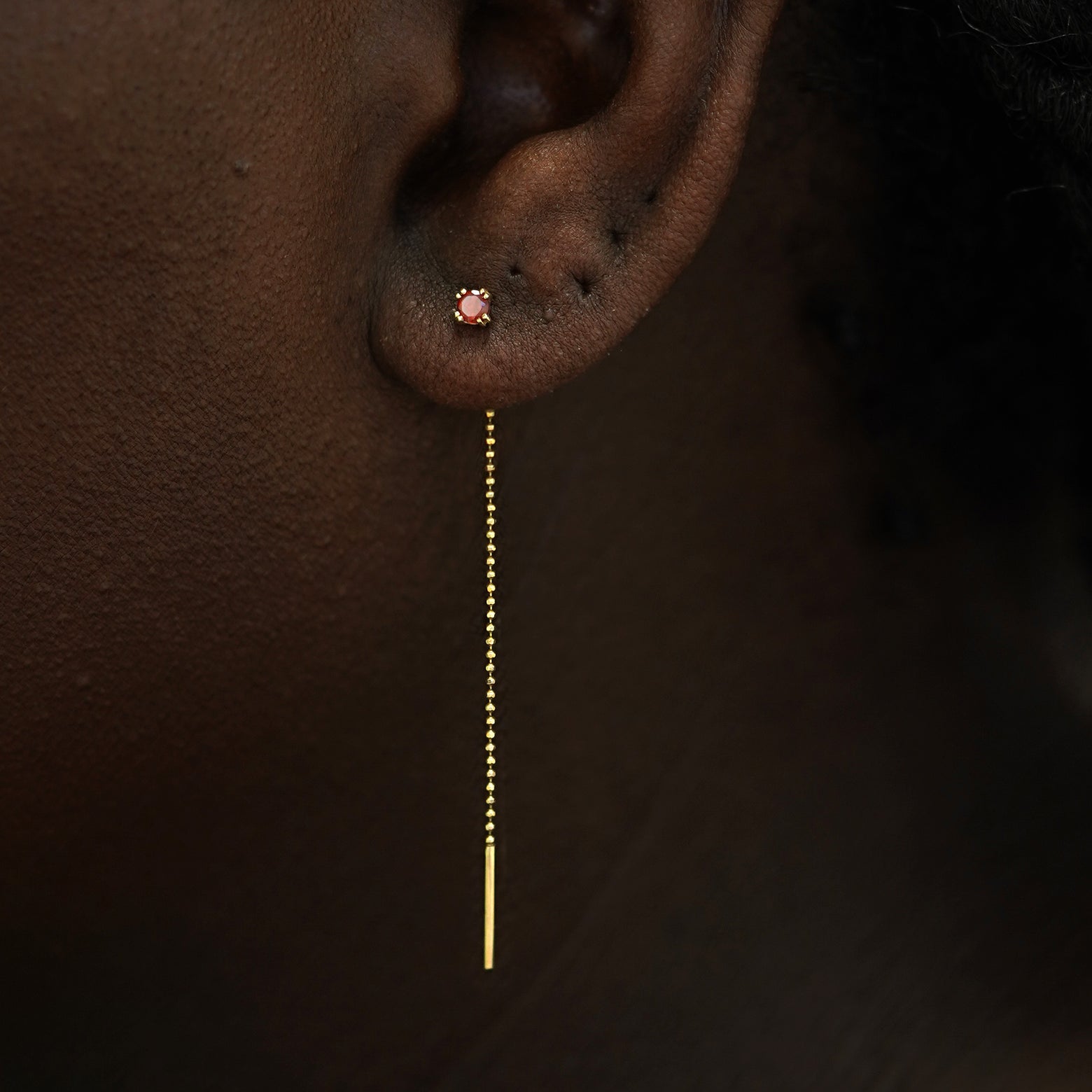 Close up view of a model's ear wearing a 14k gold garnet Gemstone Ear Threader Earring
