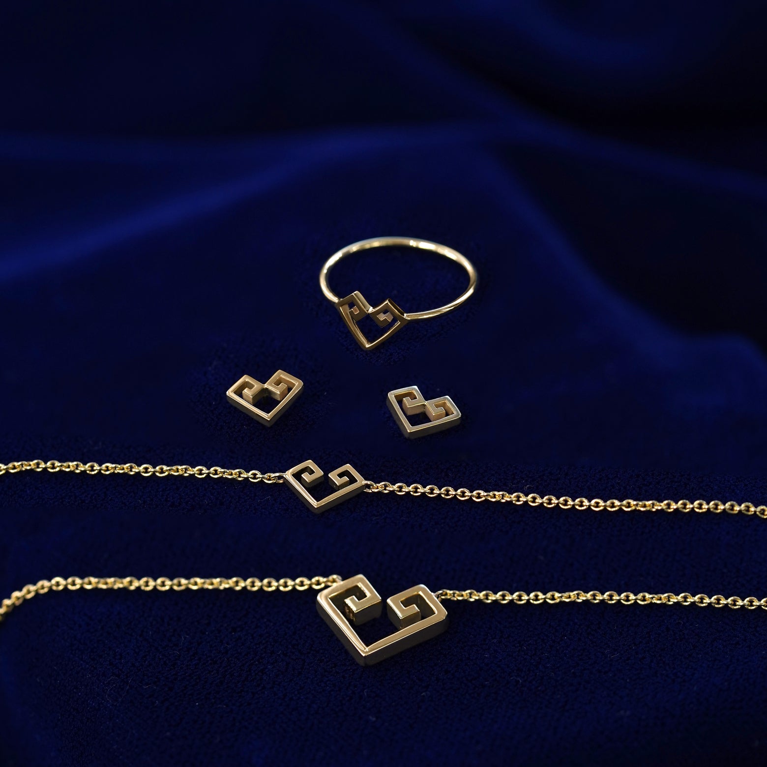 Yellow gold Chere heart ring, earrings, small and large necklaces sitting on a dark blue cloth