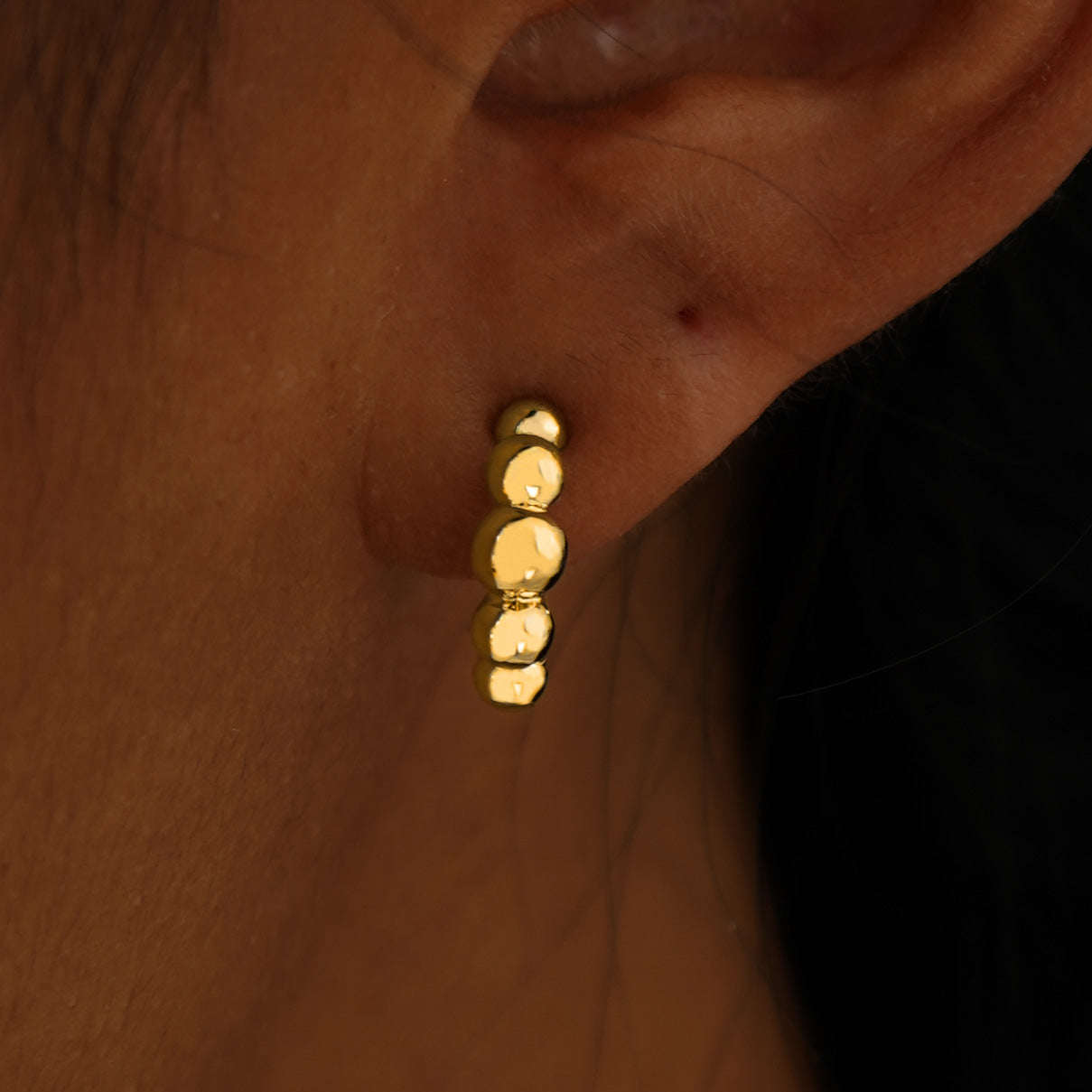 Close up view of a model's ear wearing a 14k yellow gold Graduated Puffy Beaded Hoop