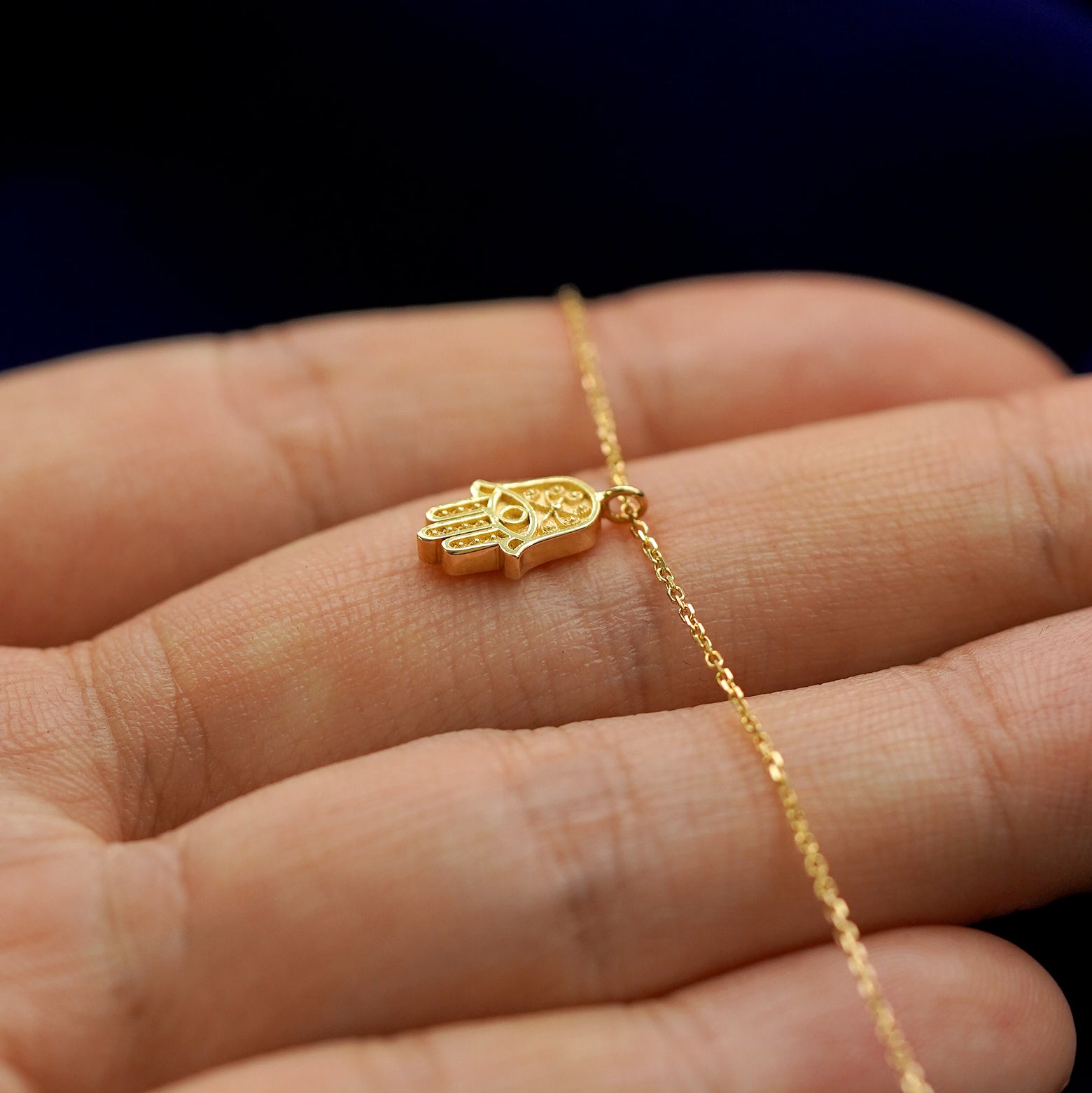 Front side view of a 14k gold hamsa pendant necklace lying across a model's fingertips