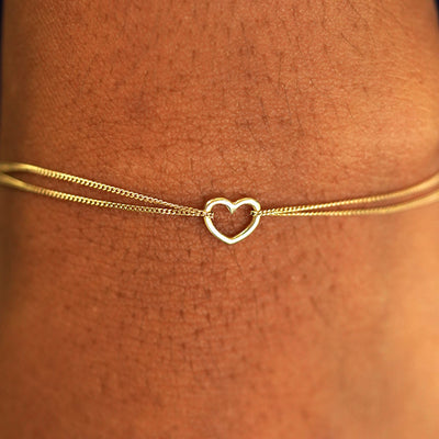 Close up view of a model's wrist wearing a solid yellow gold Heart Braceletv