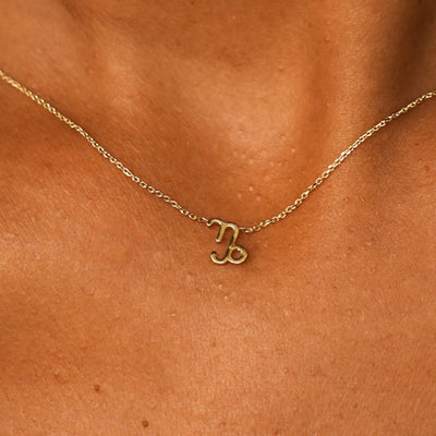 Close up view of a model's neck wearing a solid 14k yellow gold Capricorn Horoscope Necklace
