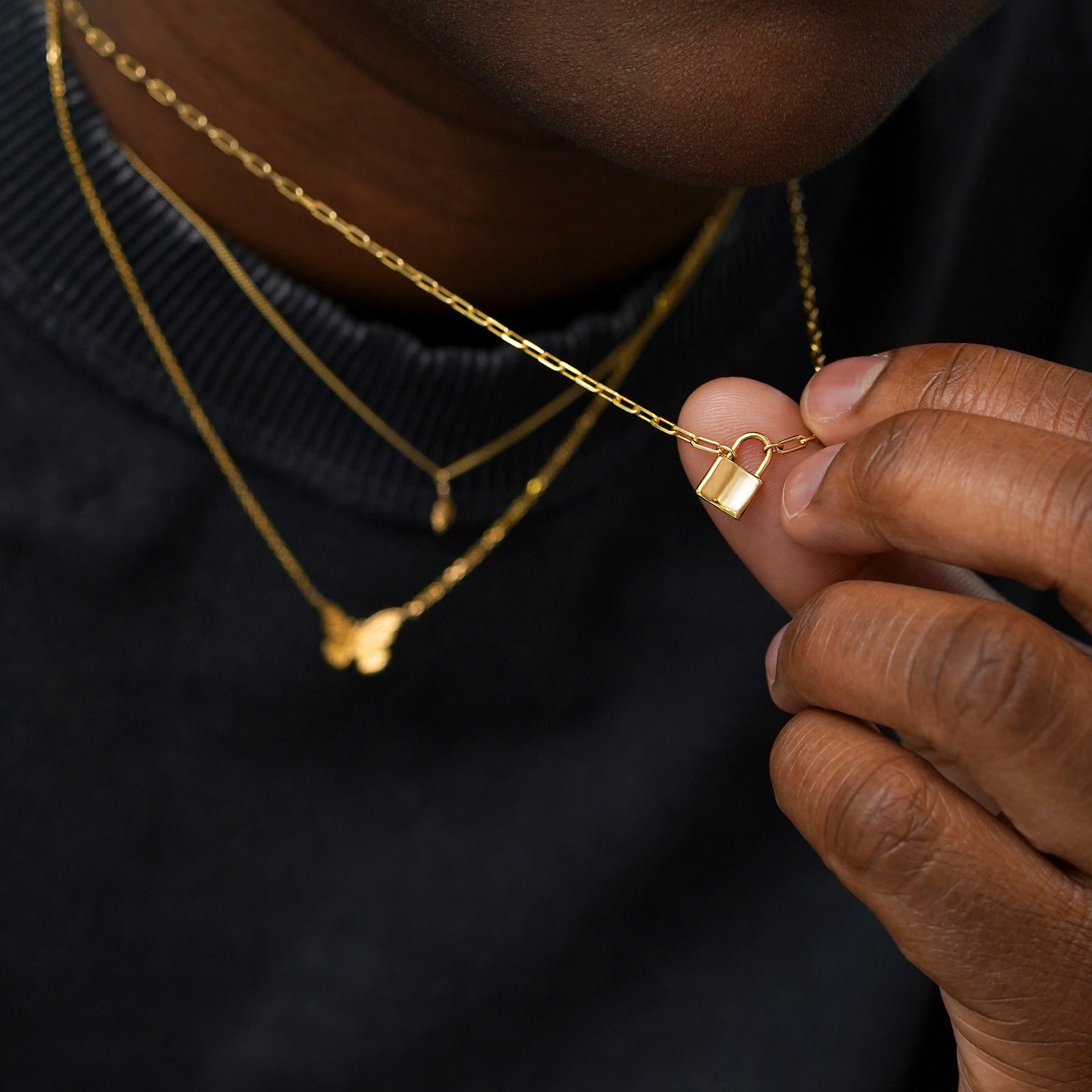 A model wearing solid 14k yellow gold Leaf, Butterfly, and Lock Necklaces while holding the lock pendant