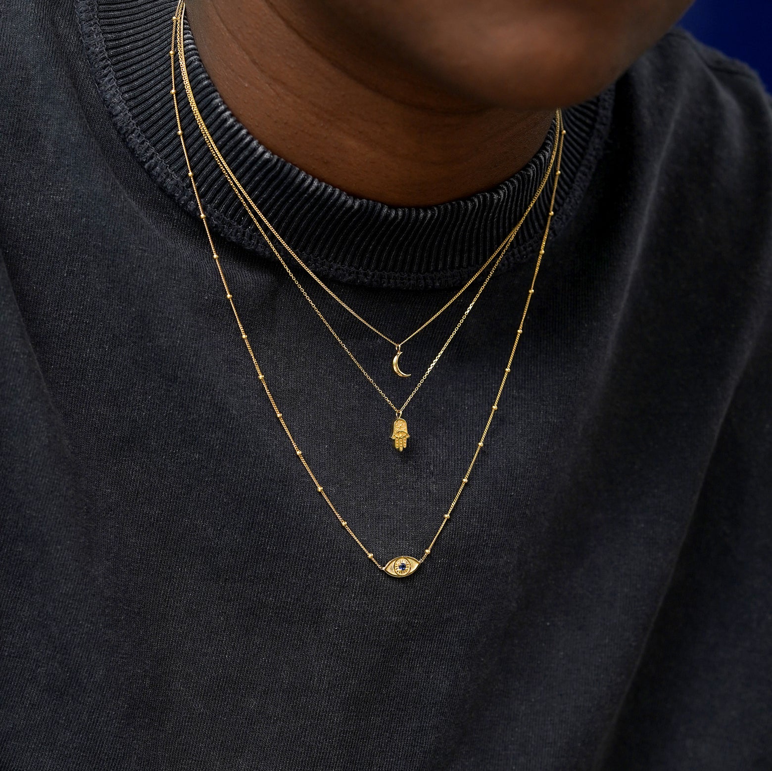 A model wearing solid 14k yellow gold Moon, Hamsa, and Gemstone Evil Eye Necklaces layered