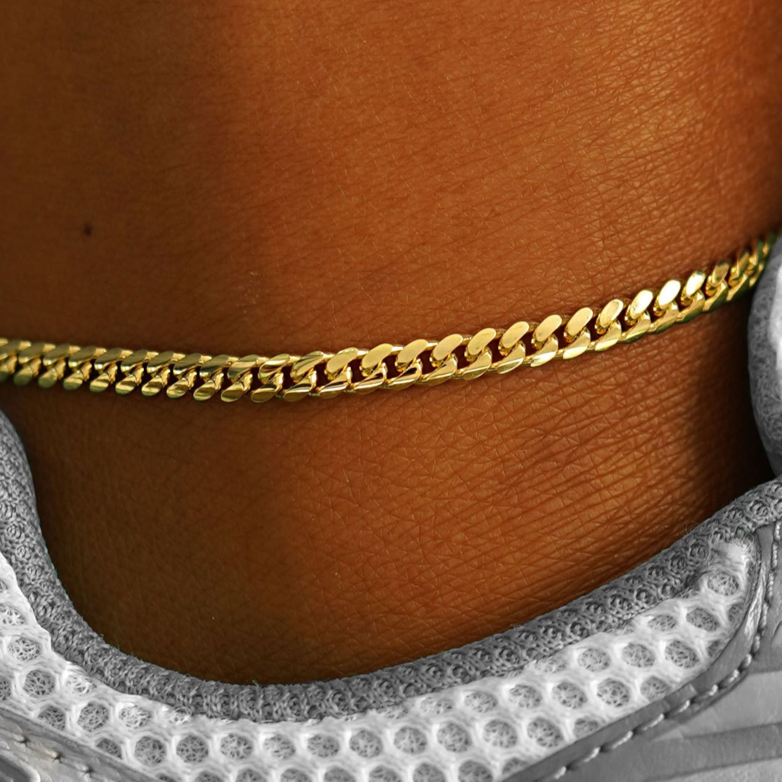 A close up view of model's ankle wear a 14k yellow gold Medium Miami Anklet