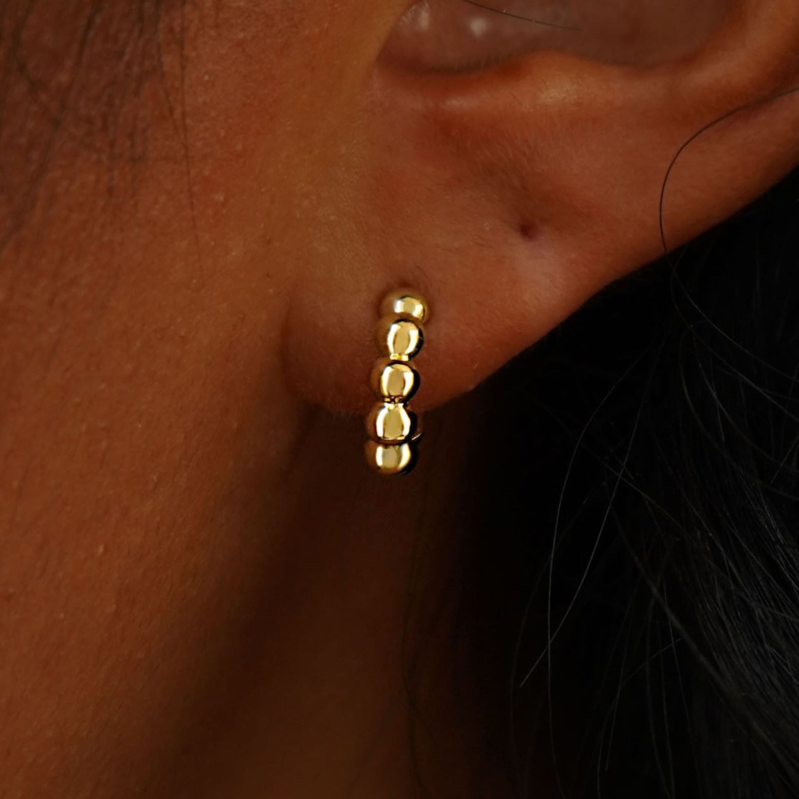 Close up view of a model's ear wearing a 14k yellow gold Mini Puffy Beaded Hoop