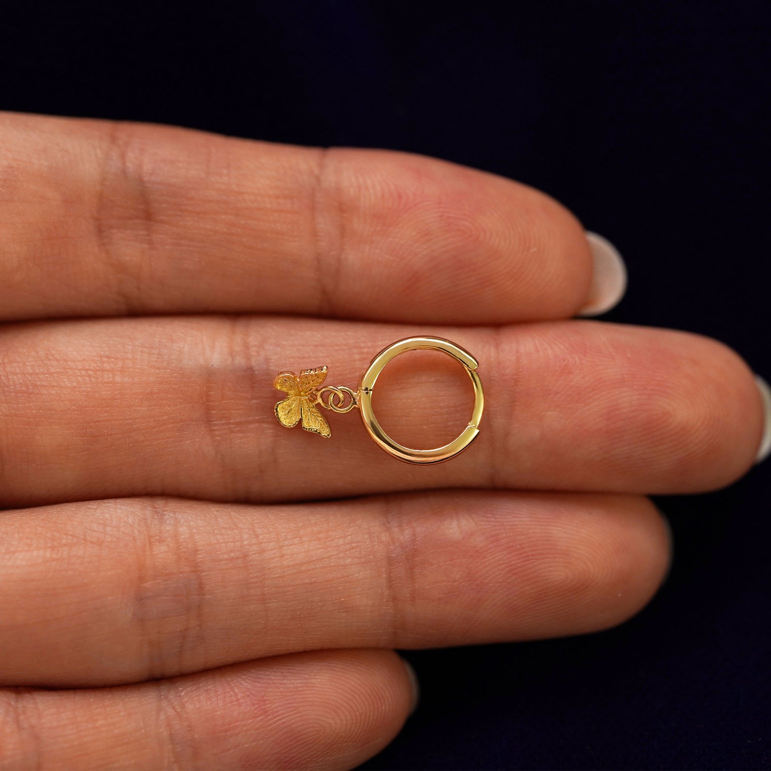 A solid 14k yellow gold Mini Butterfly Dangle Huggie Hoop closed on a model's fingertips