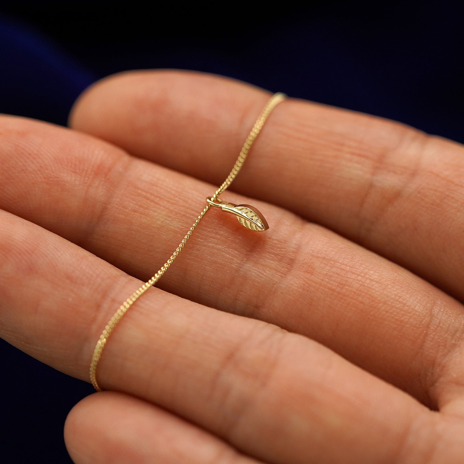 A 14k gold mini leaf pendant necklace held across a model's fingertips to show details 