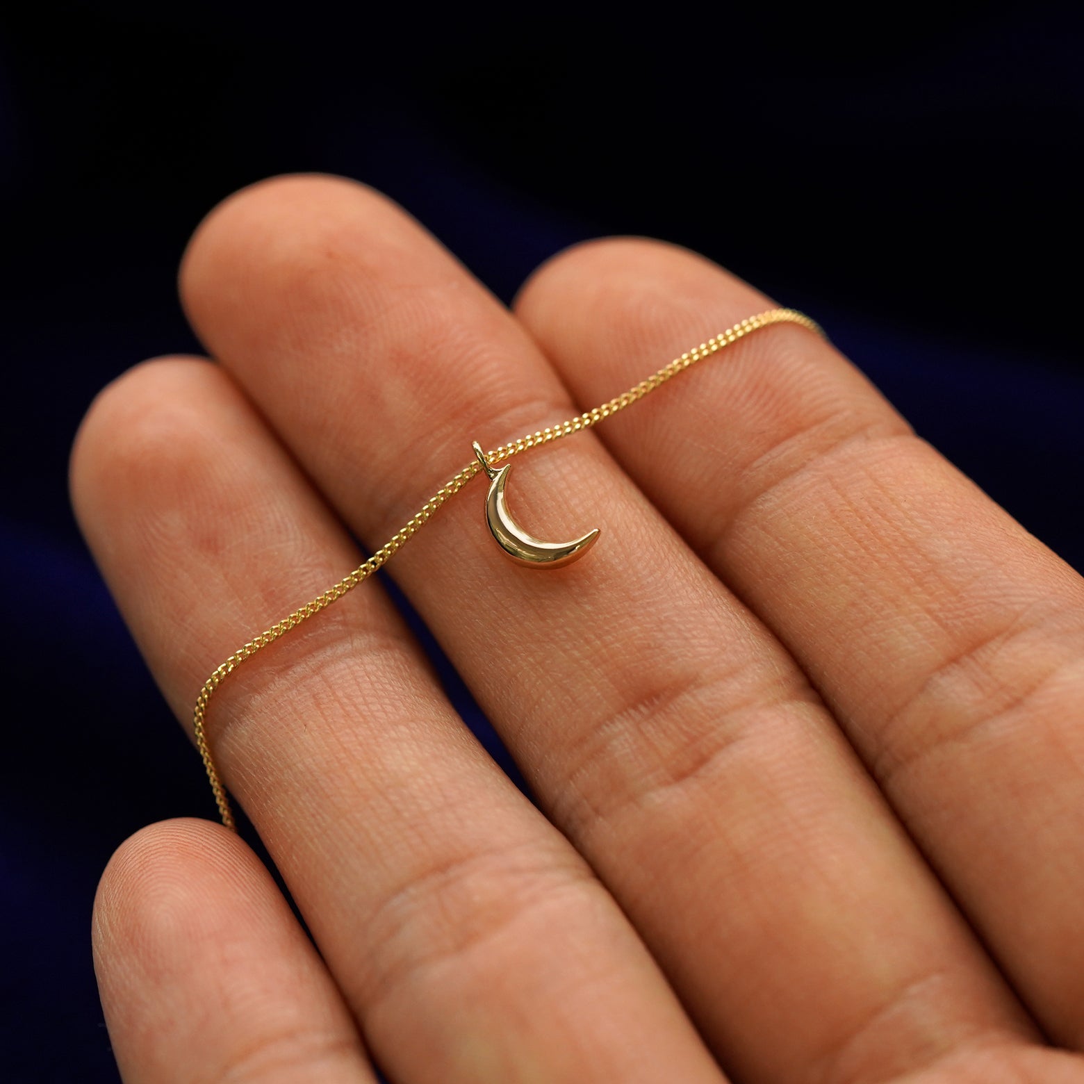 A 14k gold moon pendant necklace held across a model's fingertips to show details 