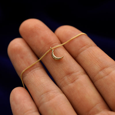 A 14k gold moon pendant necklace held across a model's fingertips to show details 