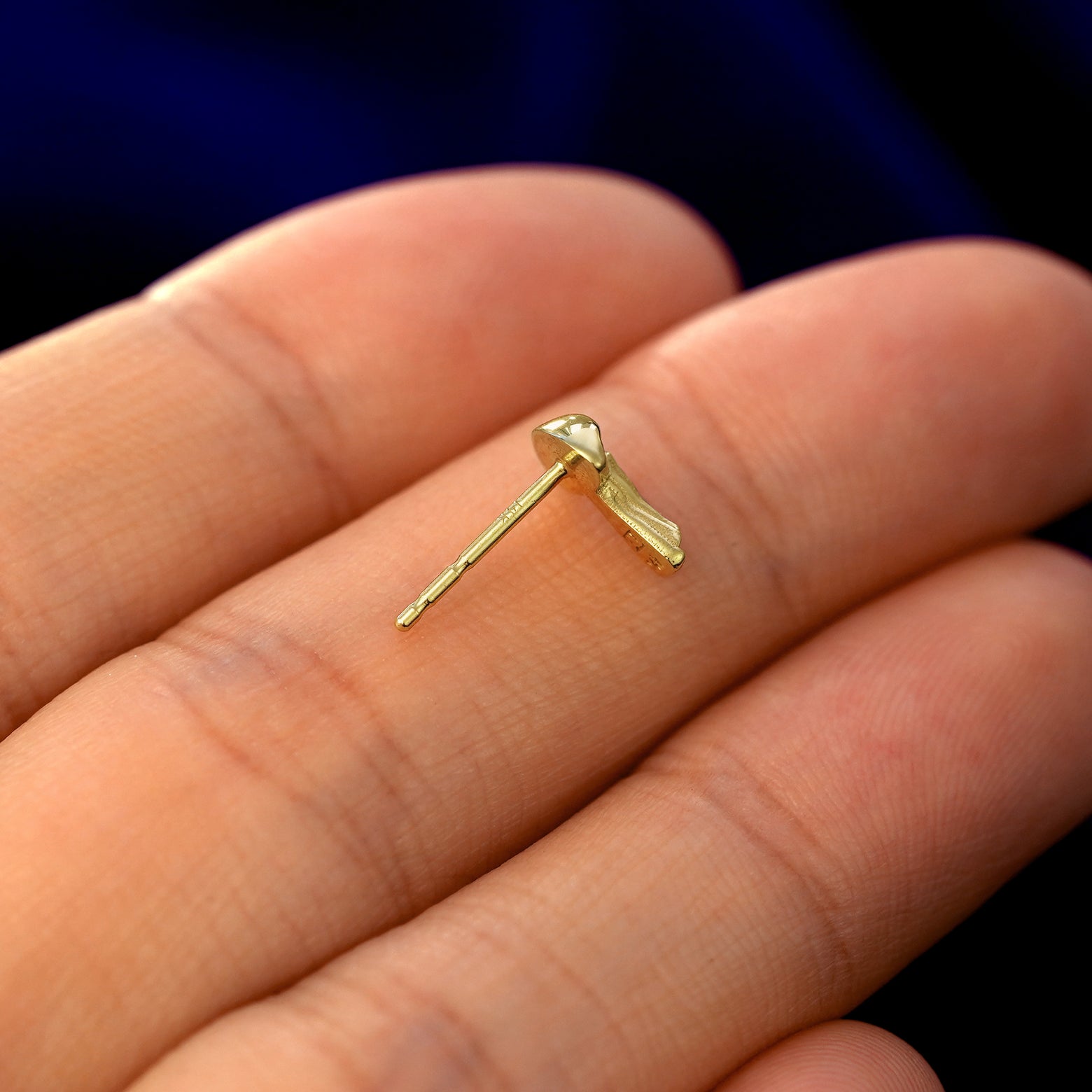 A 14k gold Mushroom Earring in a model's hand resting on its side to show the thickness of the earring 