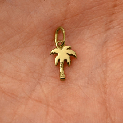 Back view of a solid 14k yellow gold Palm Tree Charm resting on in the palm of a model's hand