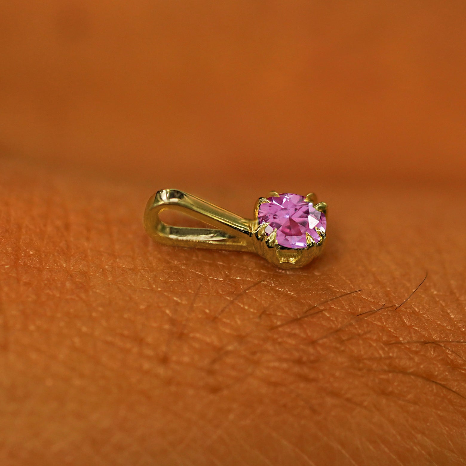A 14k yellow gold Pink Sapphire Charm for chain resting on the back of a model's hand