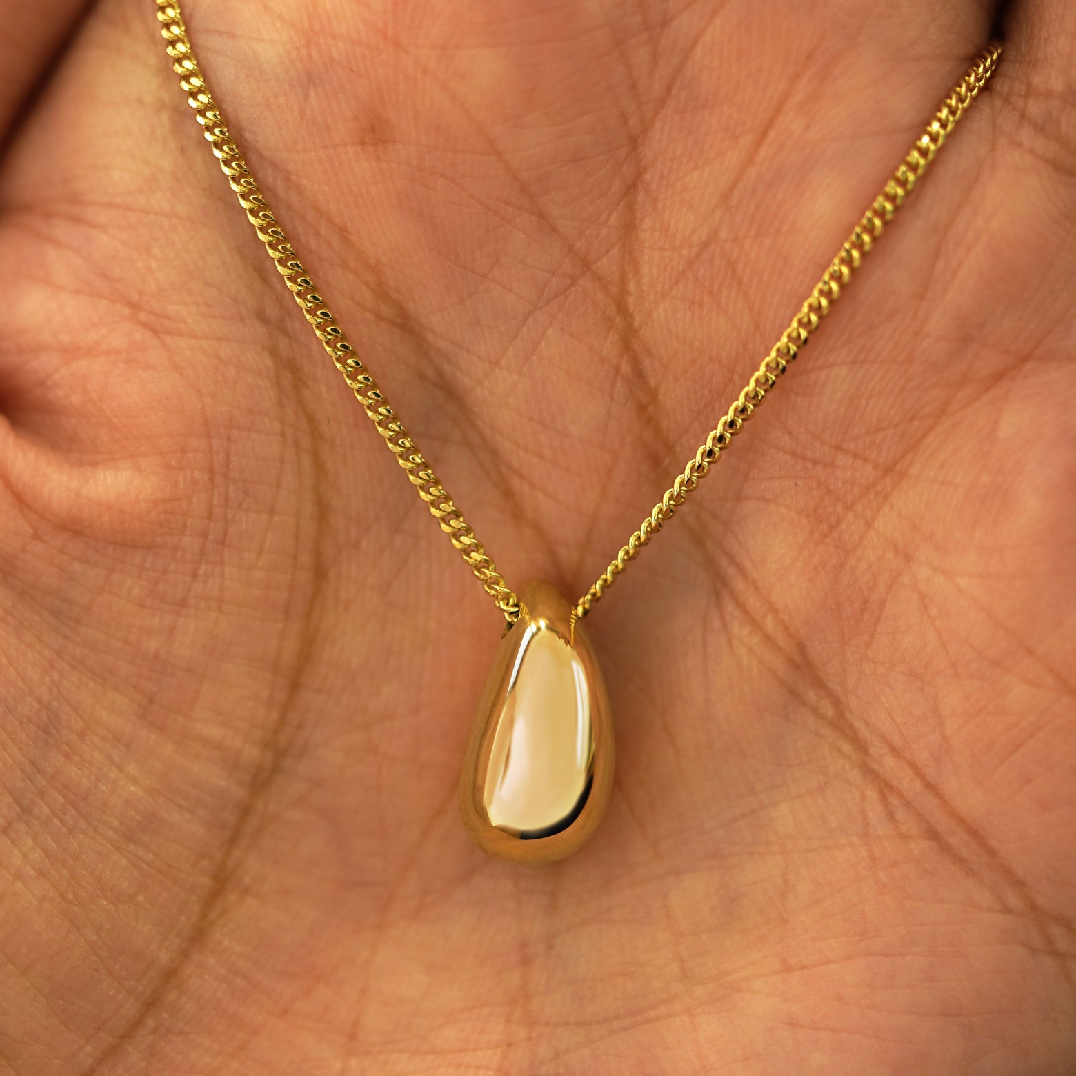 A yellow gold Puffy Teardrop Necklace draped on a model's palm
