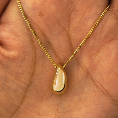 A yellow gold Puffy Teardrop Necklace draped on a model's palm