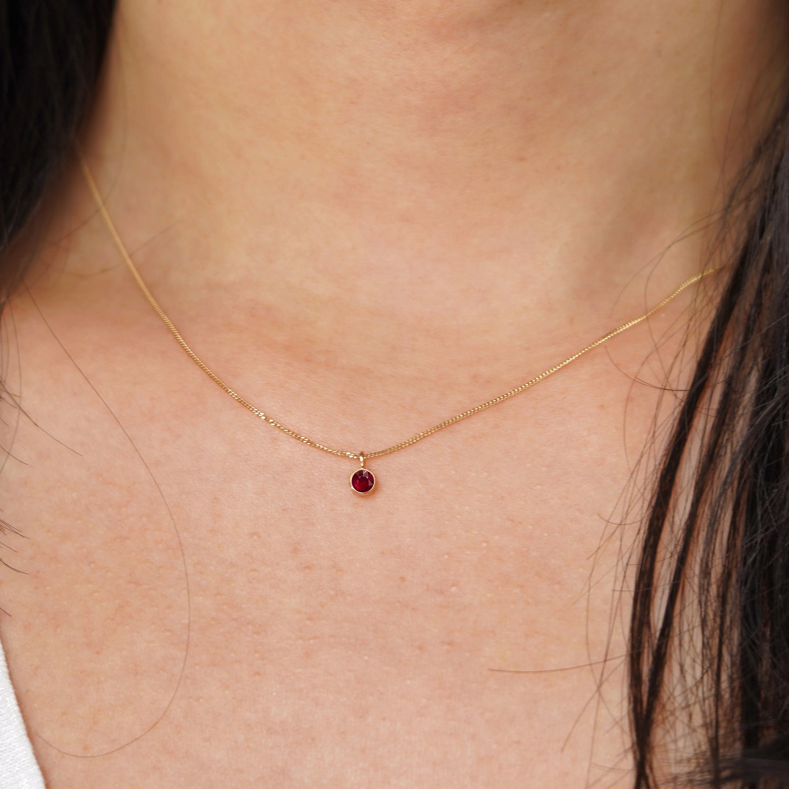 A model's neck wearing a solid 14k yellow gold Ruby necklace