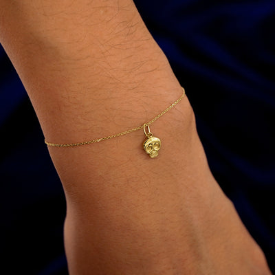 A model's wrist wearing a yellow gold Skull Skeleton Charm on a Cable Bracelet