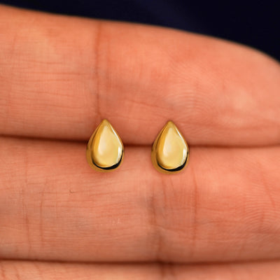 A pair of solid yellow gold Teardrop Earrings in between a model's fingers
