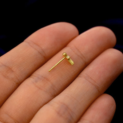 A 14k gold 3 Leaves Earring in a model's hand resting on its side to show the thickness of the earring 