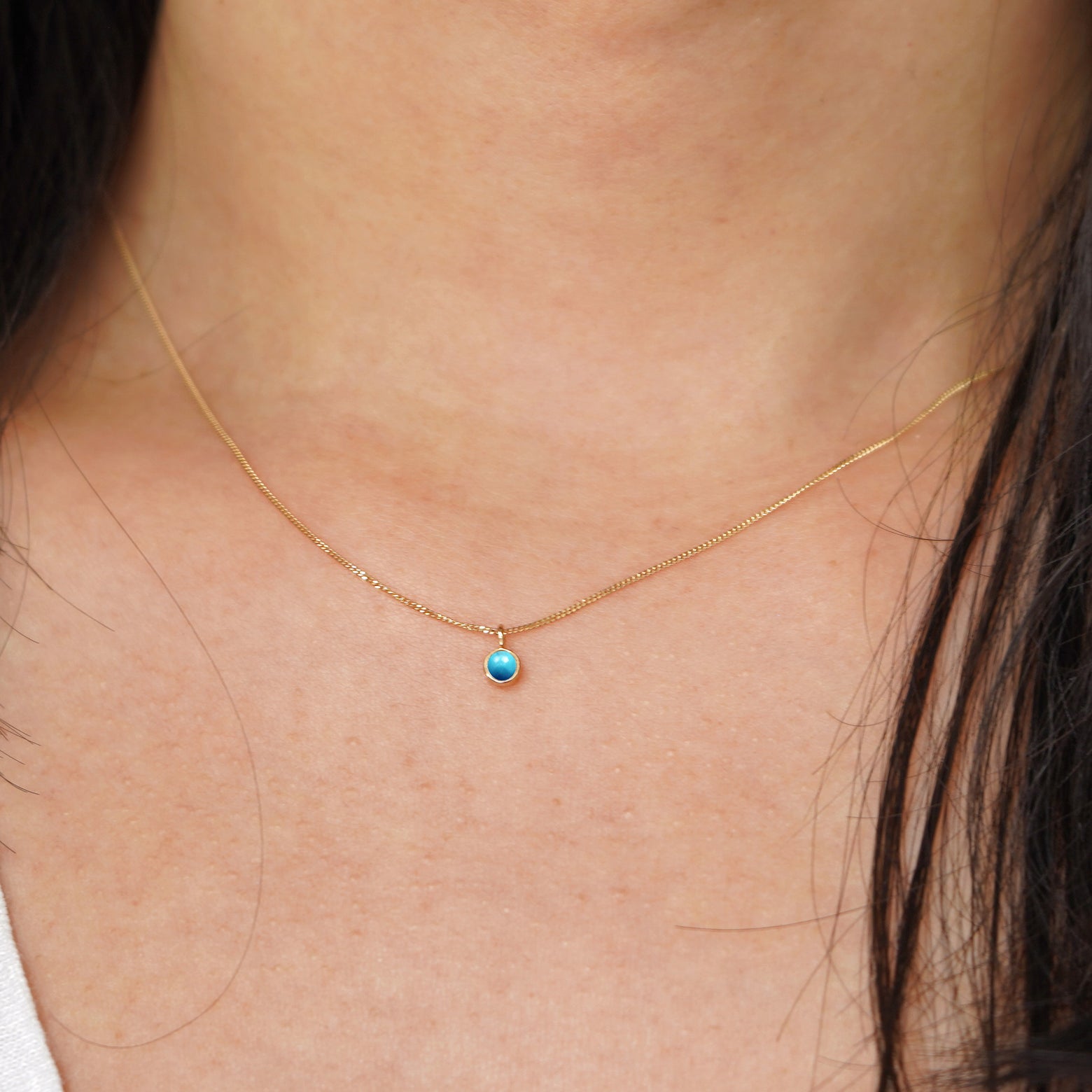 A model's neck wearing a solid 14k yellow gold Turquoise necklace