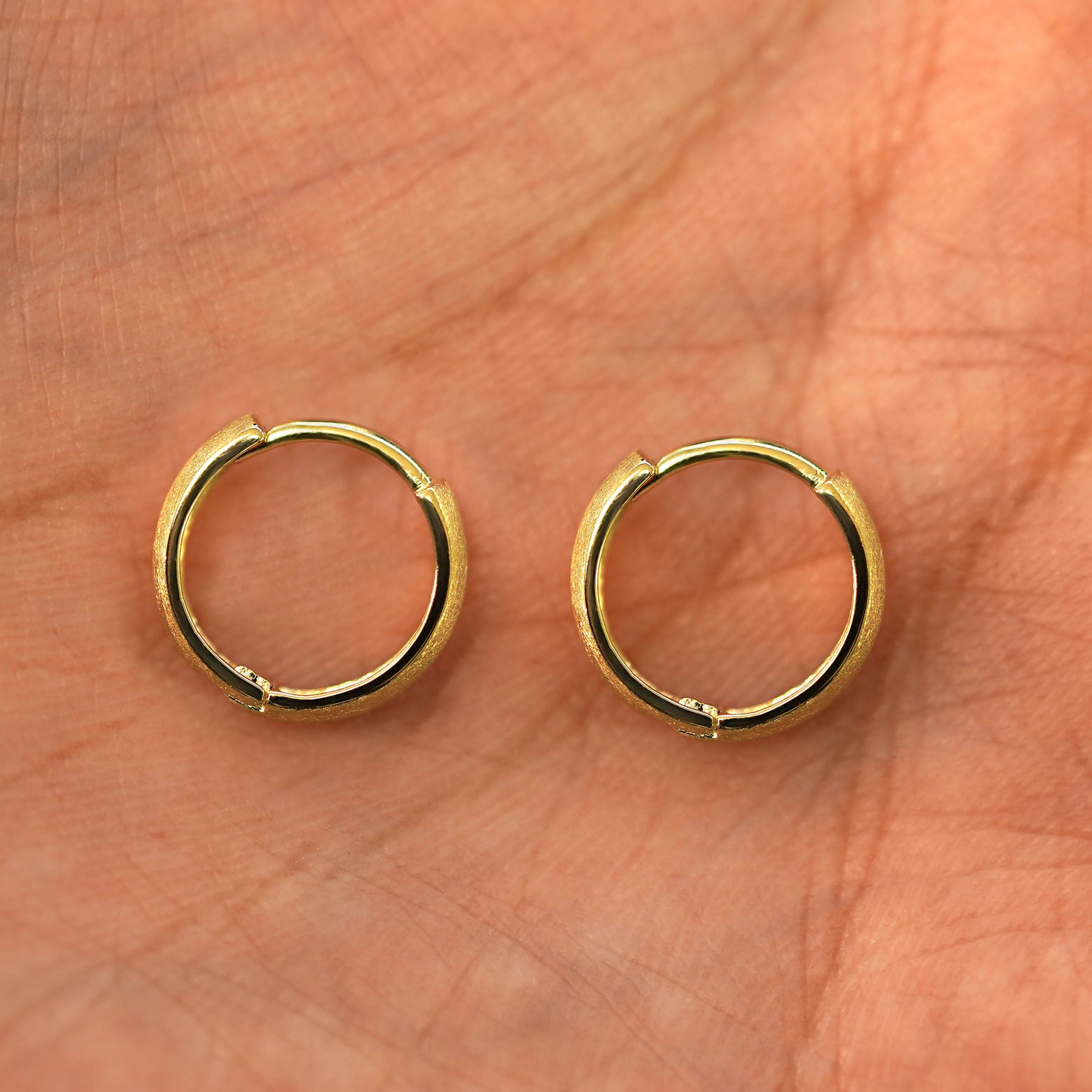 A pair of 14k gold Stardust Small Thick Huggie Hoop Earring sitting in a model's palm