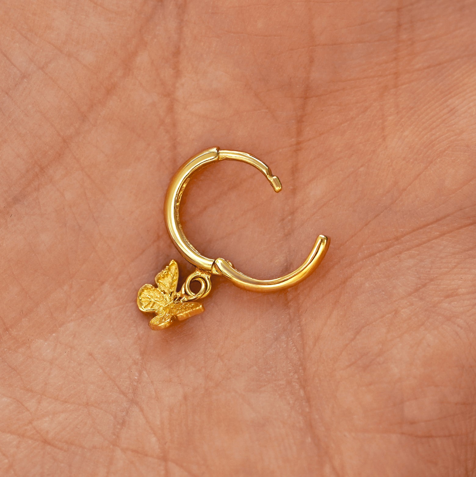 A solid 14k yellow gold Mini Butterfly Dangle Huggie Hoop Earring open a model's palm