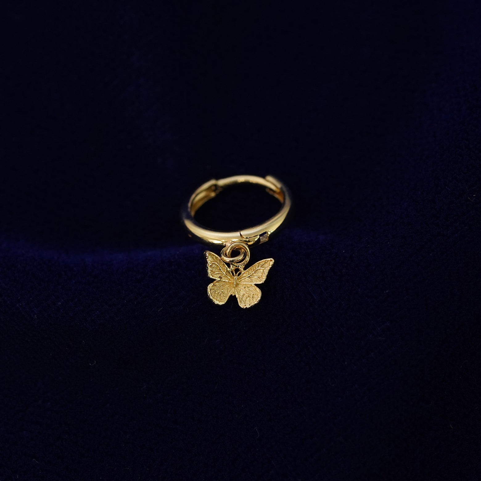 A recycled solid 14k gold Mini Butterfly Dangle Huggie Hoop earring on a dark blue background
