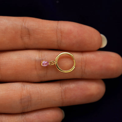 A solid 14k yellow gold Pink Sapphire Dangle Huggie Hoop closed on a model's fingertips