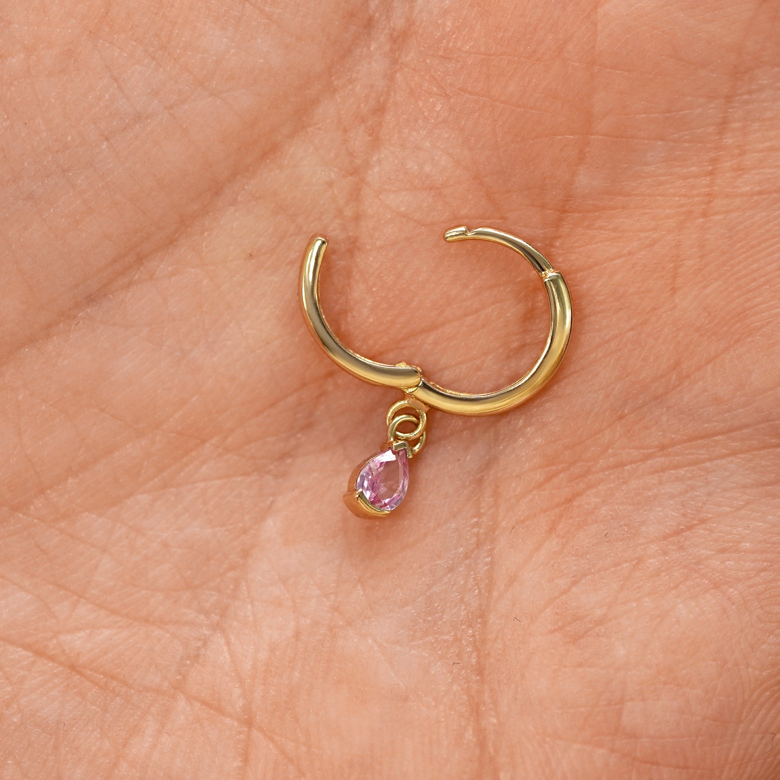 A solid 14k yellow gold Pink Sapphire Dangle Huggie Hoop Earring open a model's palm