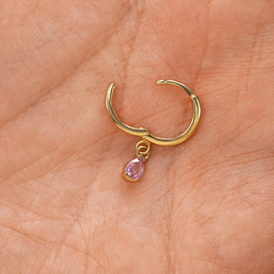 A solid 14k yellow gold Pink Sapphire Dangle Huggie Hoop Earring open a model's palm