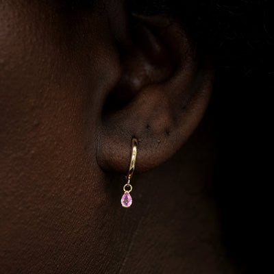 A model wearing a solid 14k gold pink pear sapphire charm hoop earring