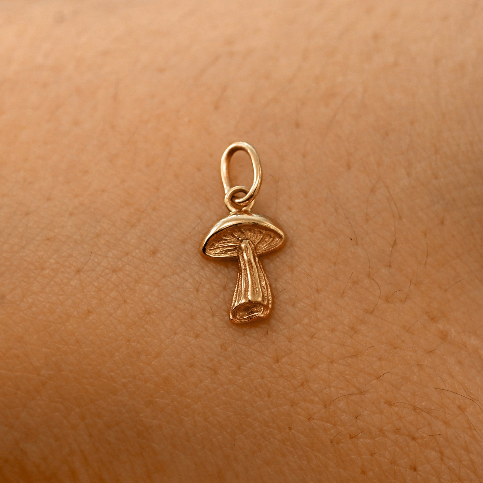 A solid 14k rose gold Mushroom Charm resting on the back of a model's hand