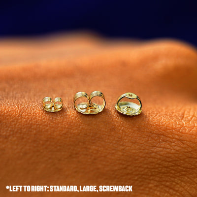 Three solid gold backing in options of screwback, large pushback, and standard pushback on the back of a hand