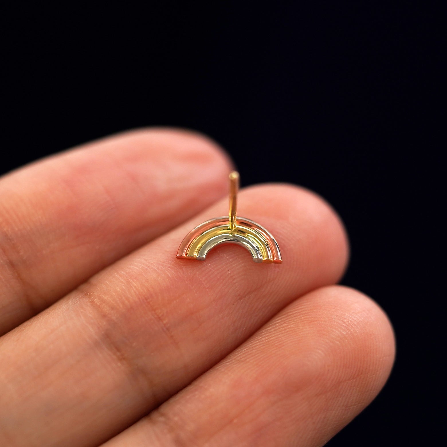 A solid gold Rainbow Earring laying facedown on a model's fingers to show the underside view