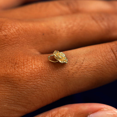 A 14k yellow gold Rose Charm for chain balancing on the back of a model's finger