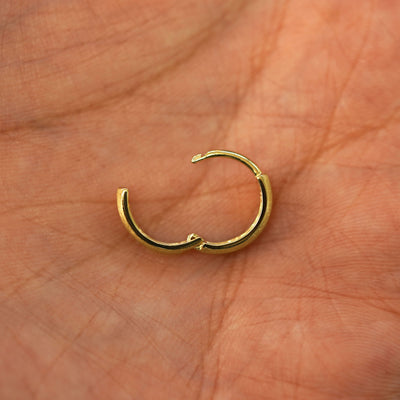 A solid 14k yellow gold Stardust Small Thick Huggie Hoop Earring open in a model's palm to show the hinge