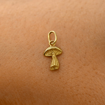 A solid 14k yellow gold Mushroom Charm resting on the back of a model's hand