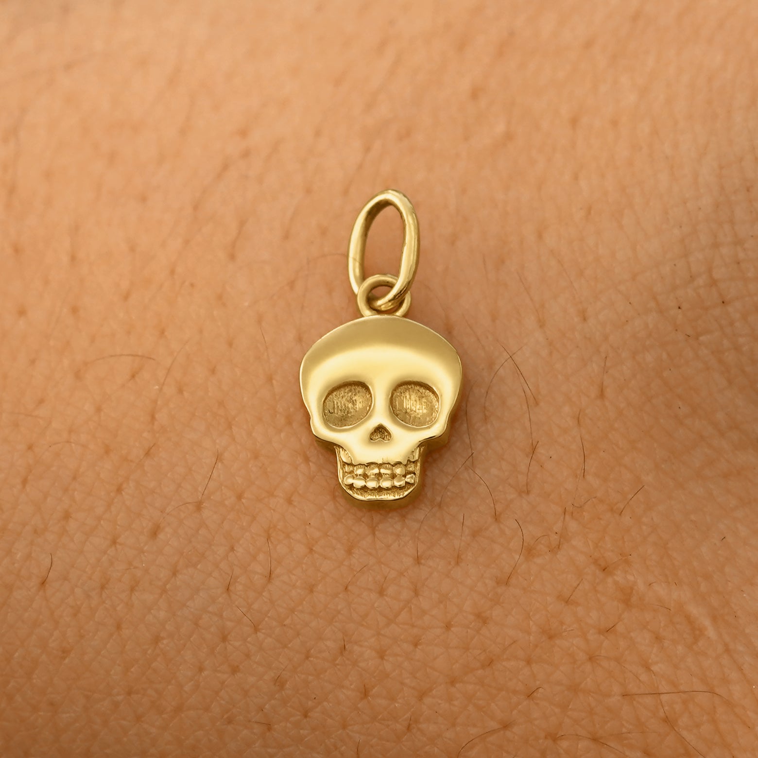 A solid 14k yellow gold Skull Charm resting on the back of a model's hand