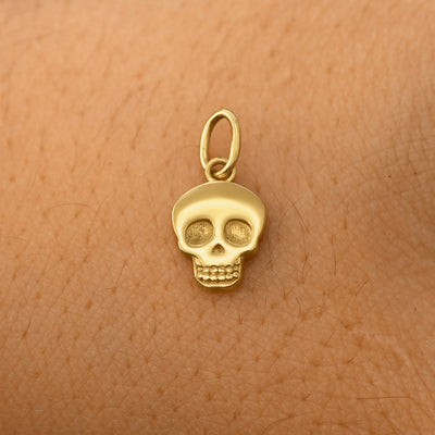 A solid 14k yellow gold Skull Charm resting on the back of a model's hand