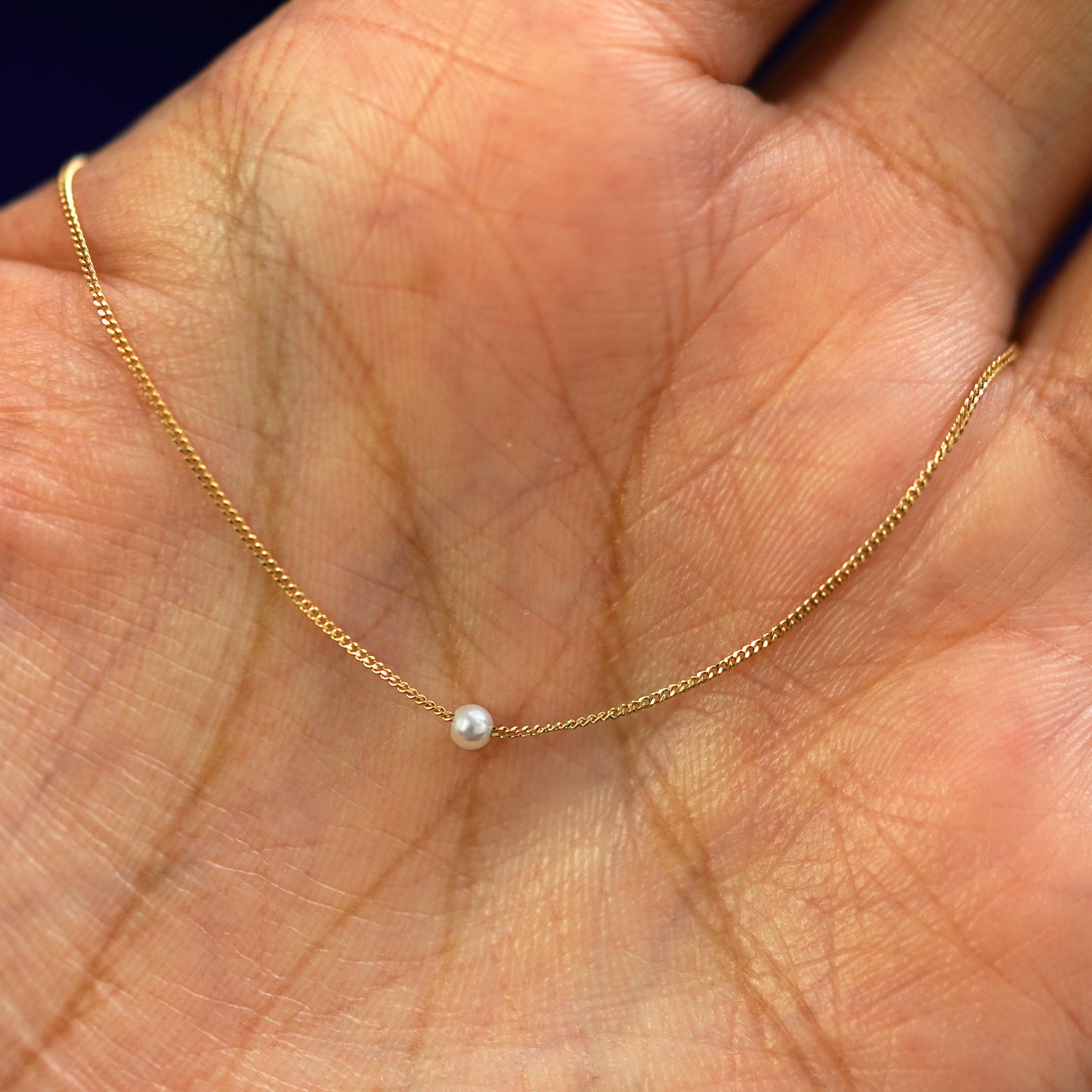 A 2mm pearl slide necklace draped on a model's palm
